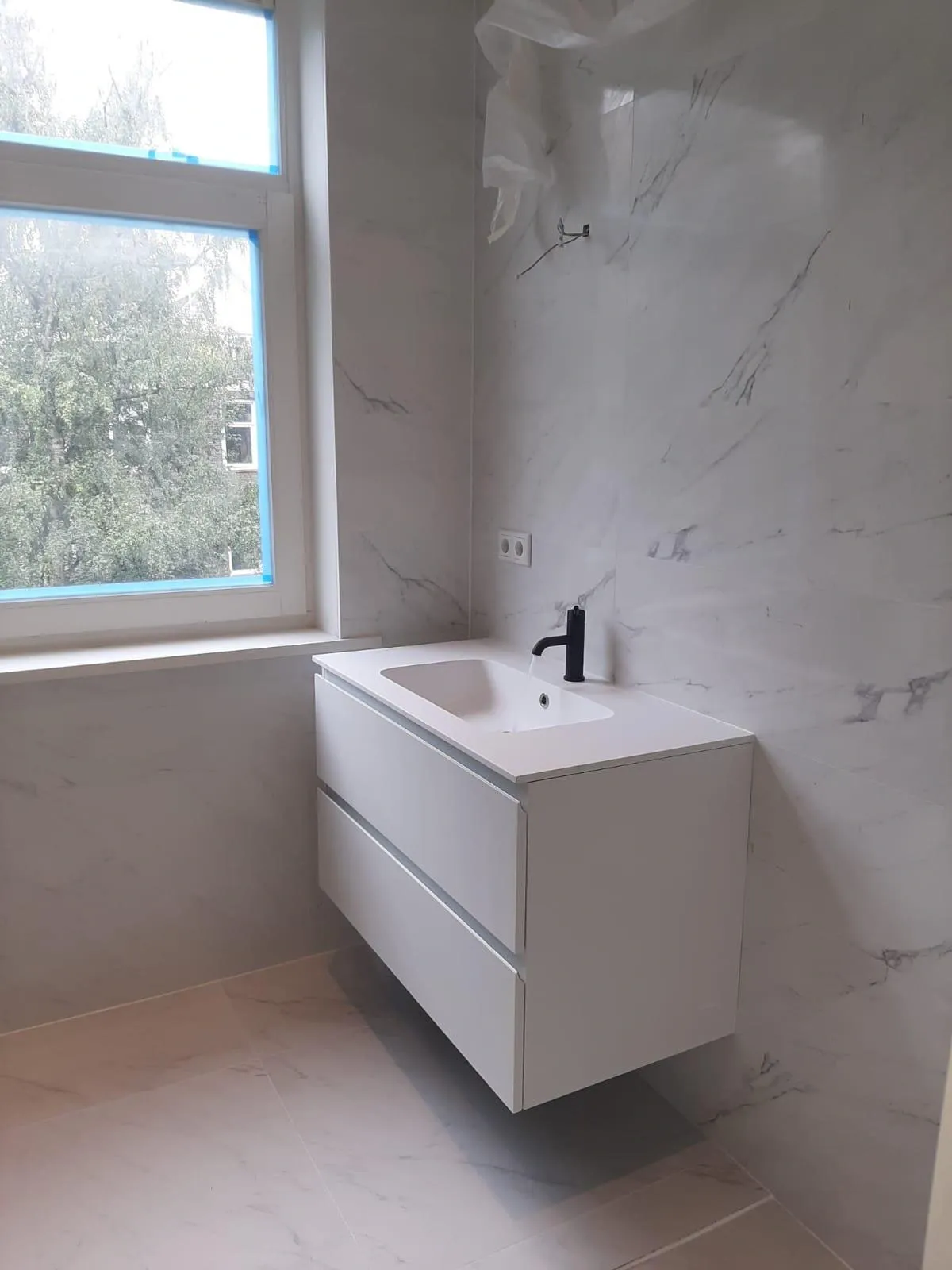 Zwevend wastafelmeubel met zwarte kraan tegen marmeren wandtegels, badkamerrenovatie Klussen Fixer